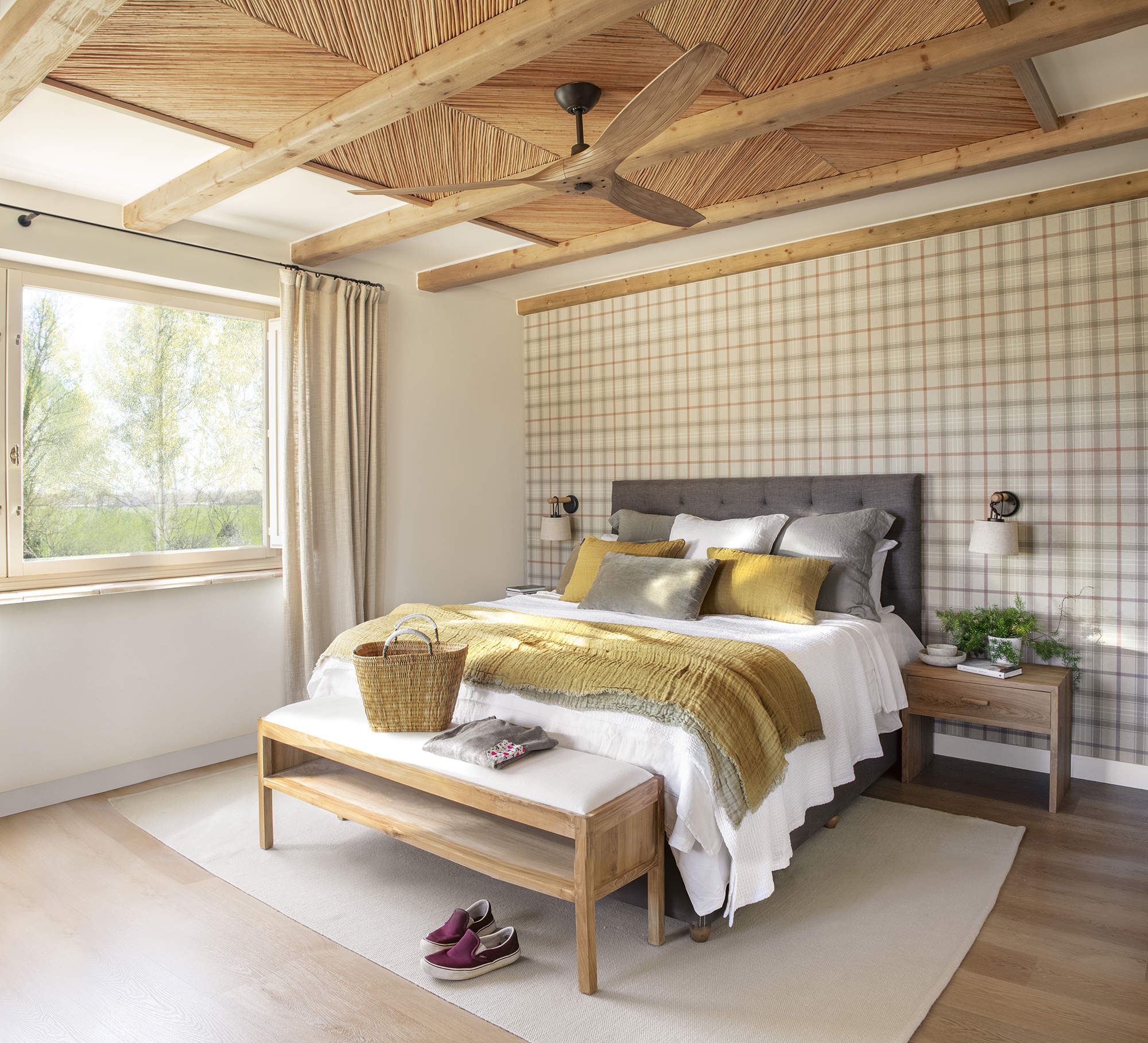 Dormitorio con pared empapelada a cuadros, cabecero de capitoné gris y ropa de cama blanca y mostaza
